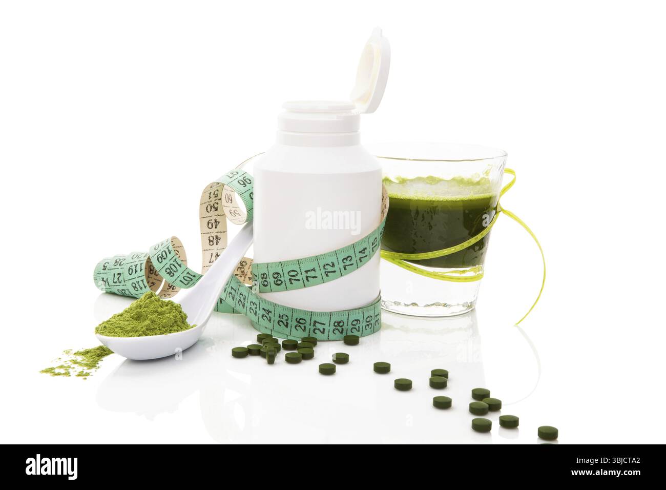 Polvere di erba, pillole di spirulina verde, vetro con agitazione vegetale verde e metro a nastro isolato su sfondo bianco. Salute verde abbraccio Foto Stock