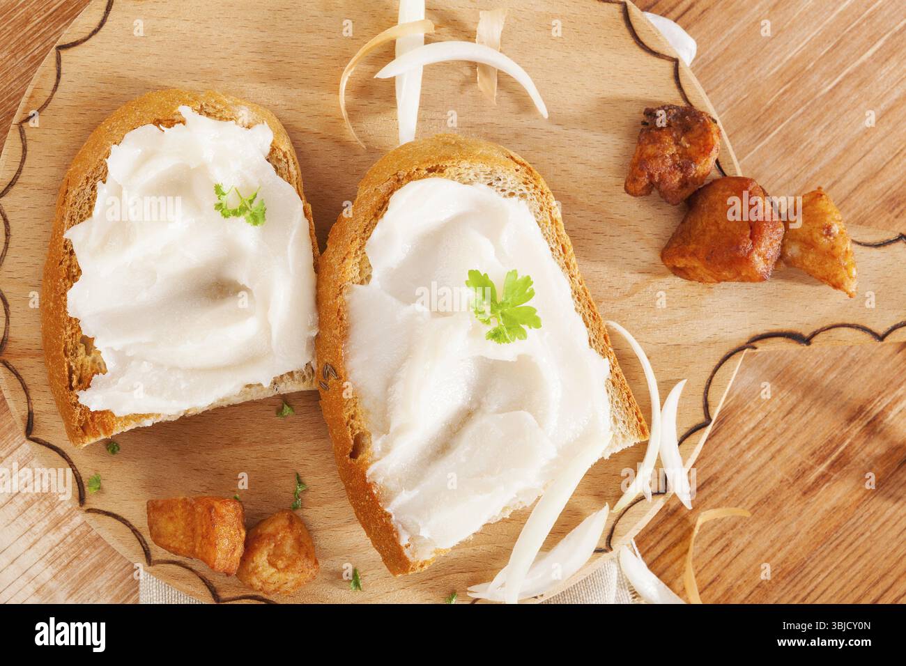 Deliziose fette di pane con strutto e graffi sulla vista dall'alto del tagliere in legno vintage. Cucina tradizionale con pane in stile country europeo Foto Stock