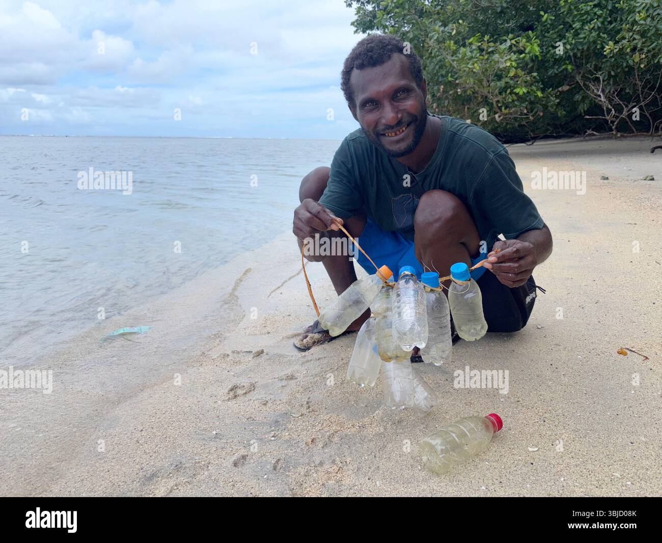 Guida locale che raccoglie bottiglie di plastica da 150 ml da riutilizzare come contenitori per olio di cocco, Tetepare, Provincia Occidentale, Isole Salomone. No MR Foto Stock
