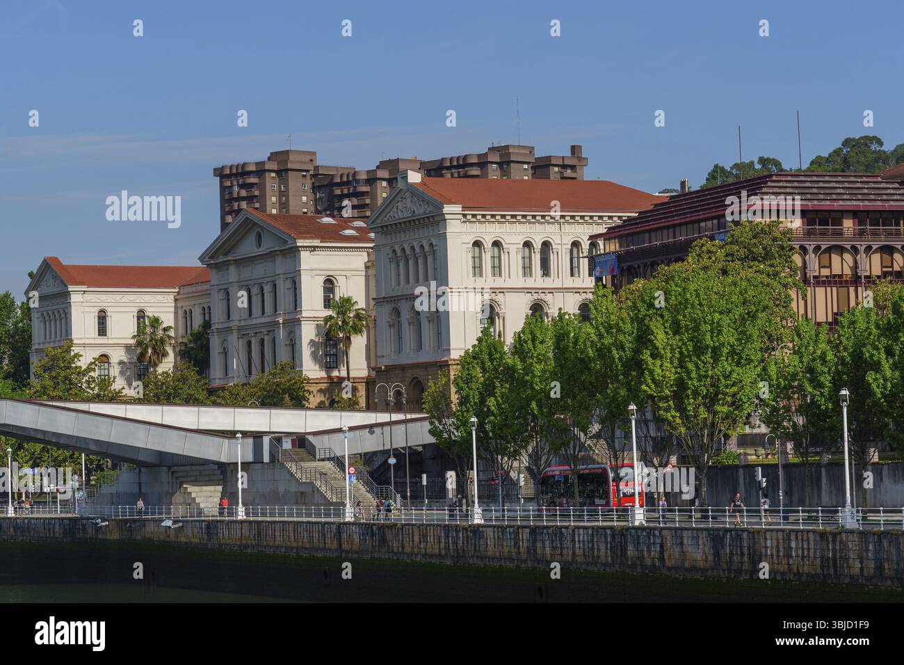 Costruzione lungo un fiume con ponte sotto un cielo limpido, Bilbao, Paesi Baschi, Spagna, Europa Foto Stock