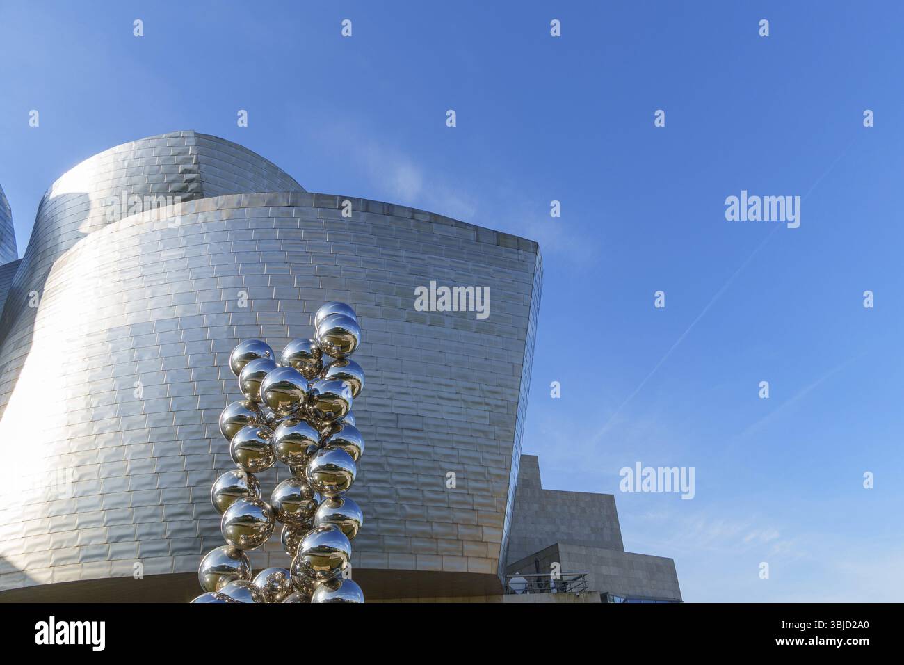 Edificio di forma metallica con scultura lucida in primo piano sotto un cielo limpido, Bilbao, Paesi Baschi, Spagna, Europa Foto Stock