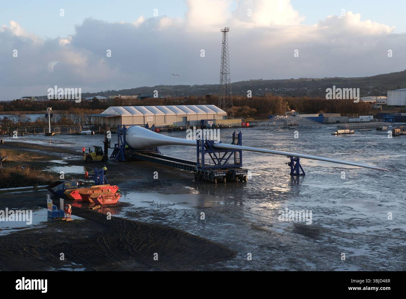 La pala della turbina eolica viene trasportata da un rimorchio modulare semovente per il caricamento mediante gru mobili sulla nave portante per carichi pesanti a Belfast. Foto Stock