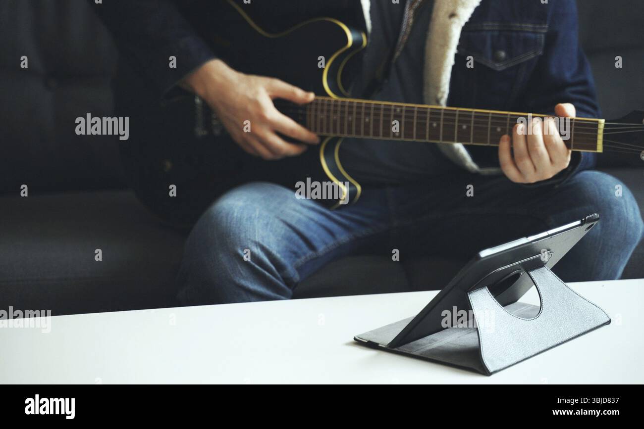 L'uomo impara a suonare la chitarra. Lezione online remota Foto Stock