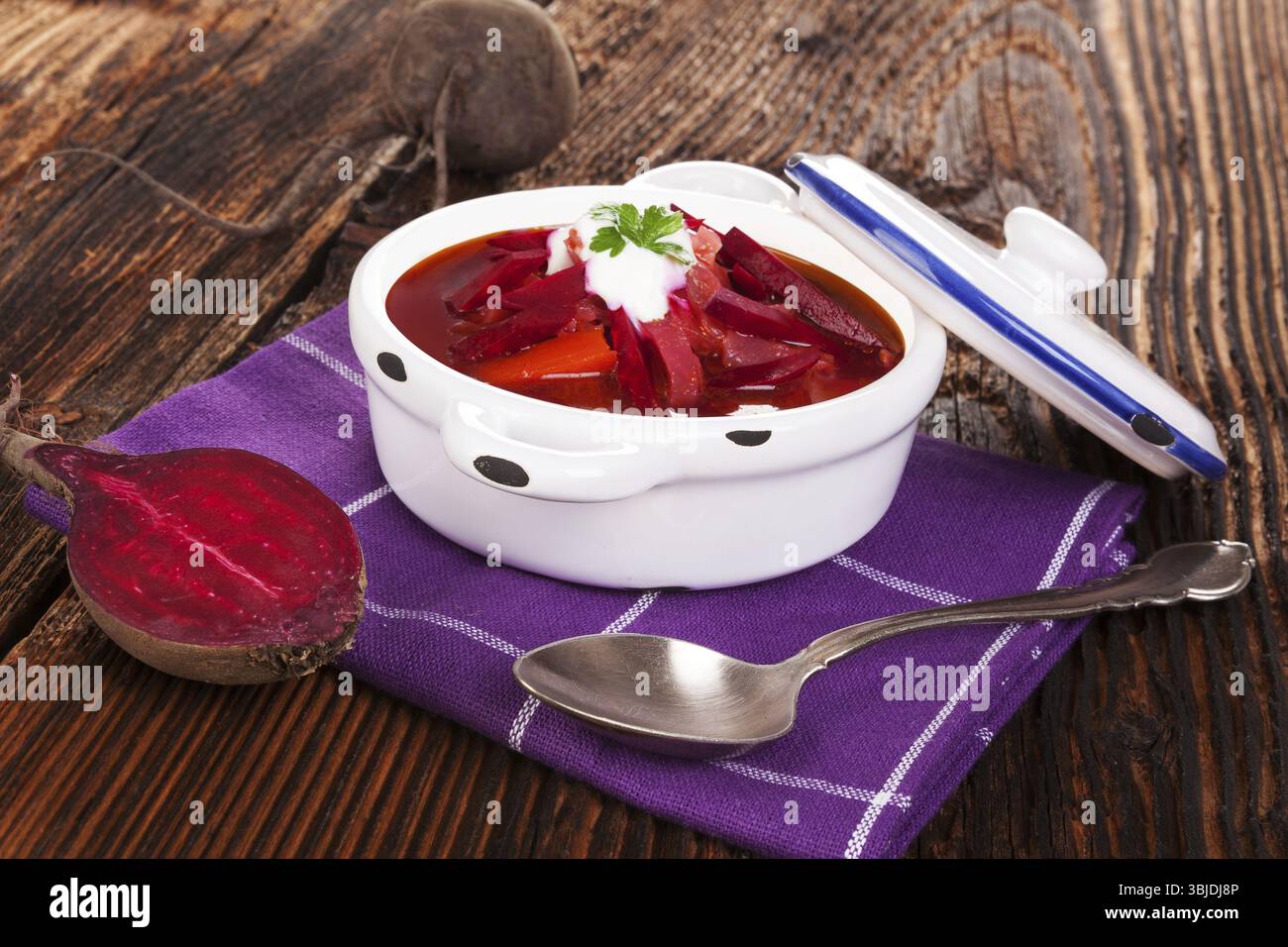 Deliziosa zuppa borsch ucraina con verdure fresche di barbabietola su un panno viola su un tavolo rustico in legno. Cucina tradizionale europea Foto Stock