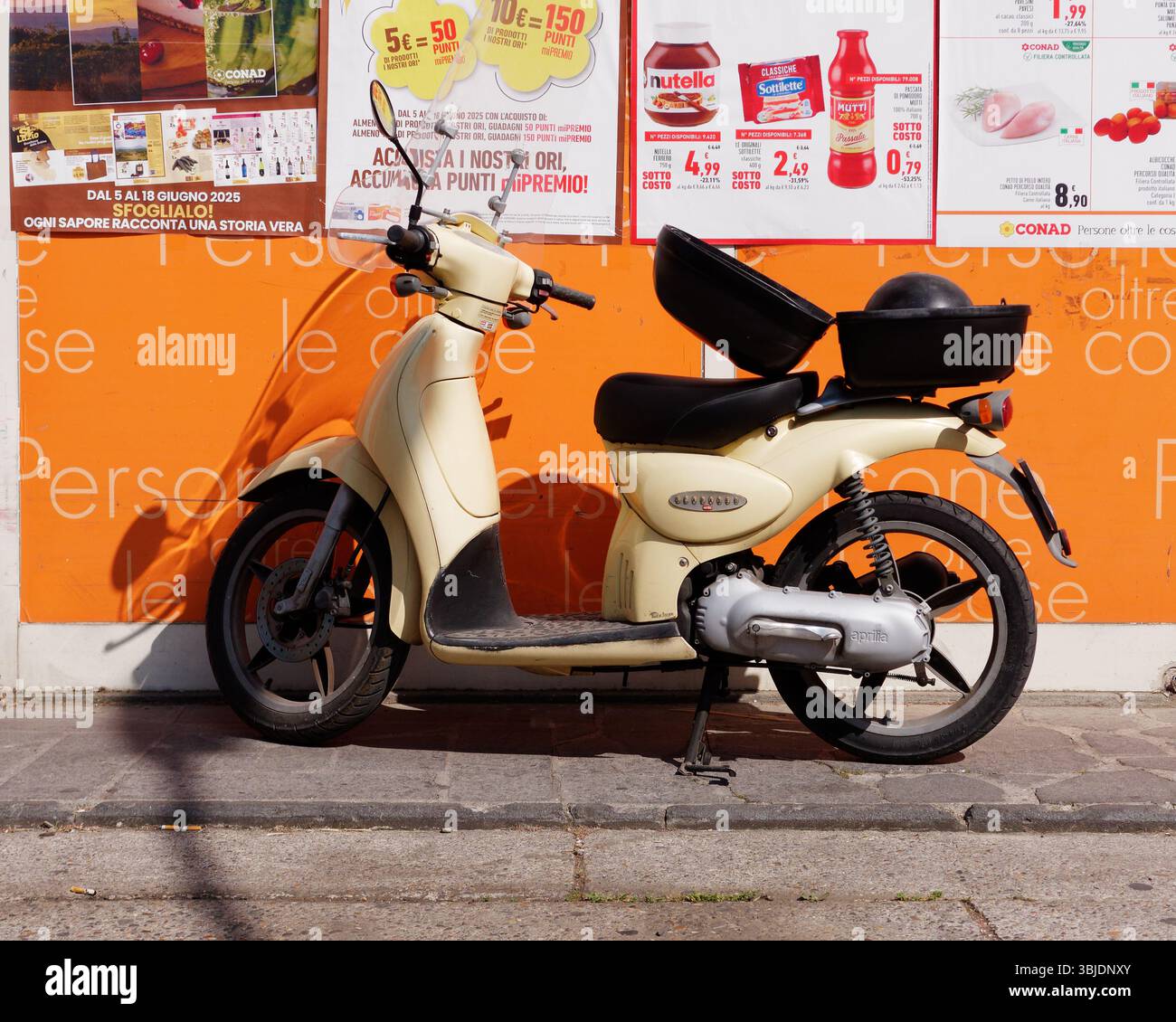 Scooter beige parcheggiato contro la parete arancione del supermercato con materiale promozionale a Montefiascone, Italia. 14 giugno 2025. Foto Stock