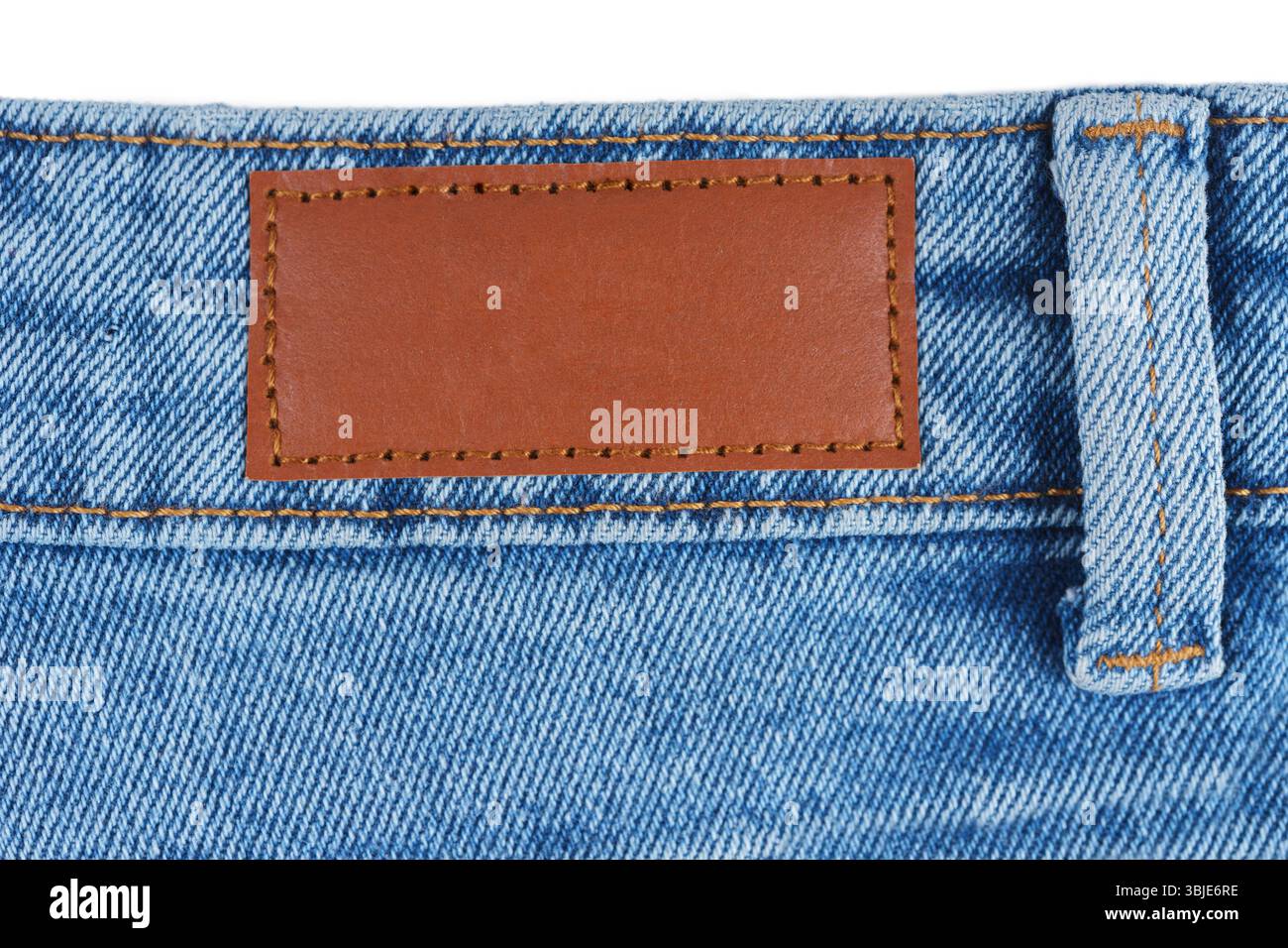 Primo piano dell'etichetta marrone in pelle cucita su jeans blu denim. Texture macro del tessuto e cuciture. Ideale per concetti di moda, tessile o branding negli annunci Foto Stock