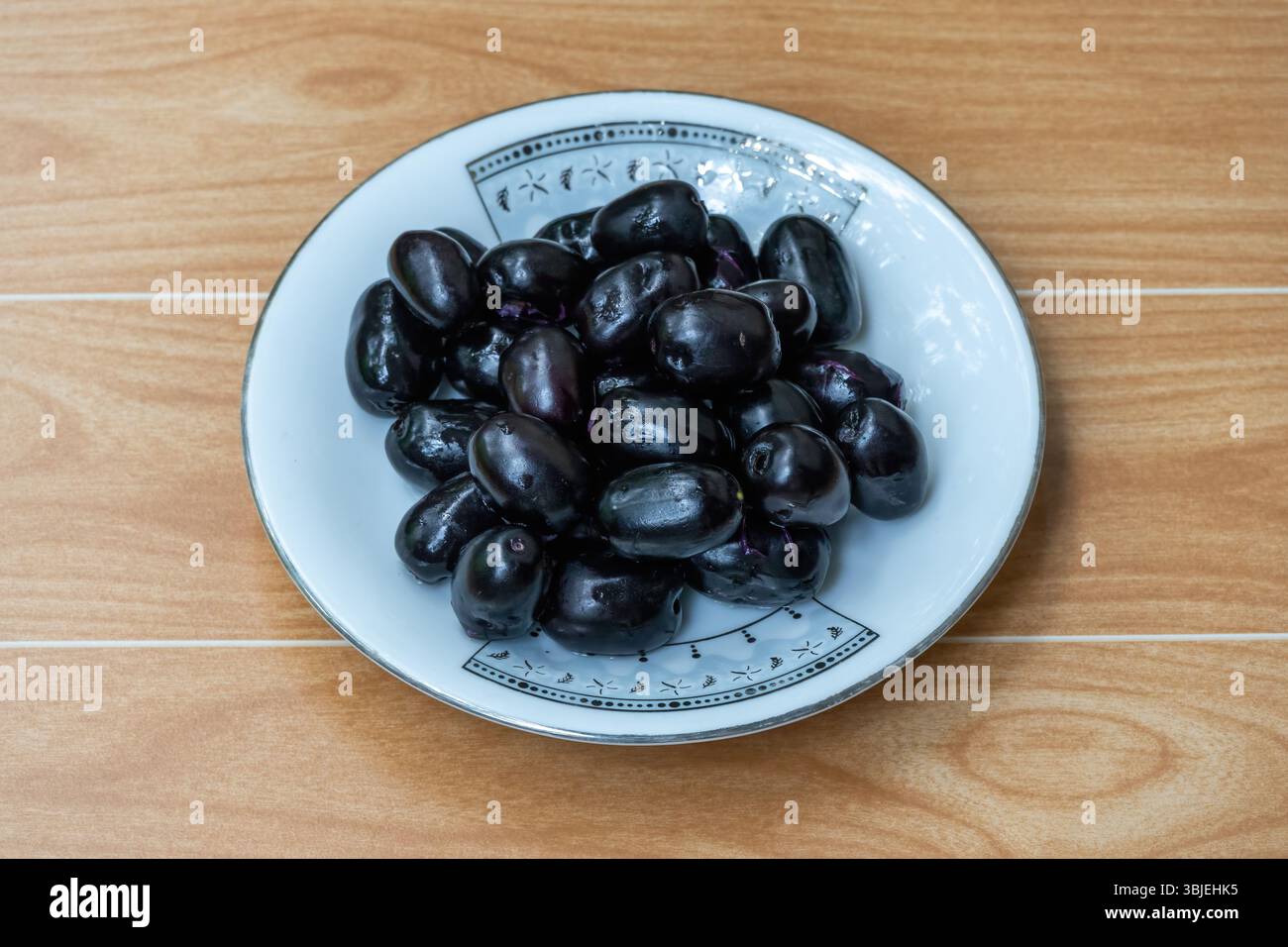 Prugne nere fresche su piatto bianco, fondo in legno. Deliziosa prugna di Giava, frutta di Jamun (Syzygium cumini) ricca di antiossidanti. Foto Stock