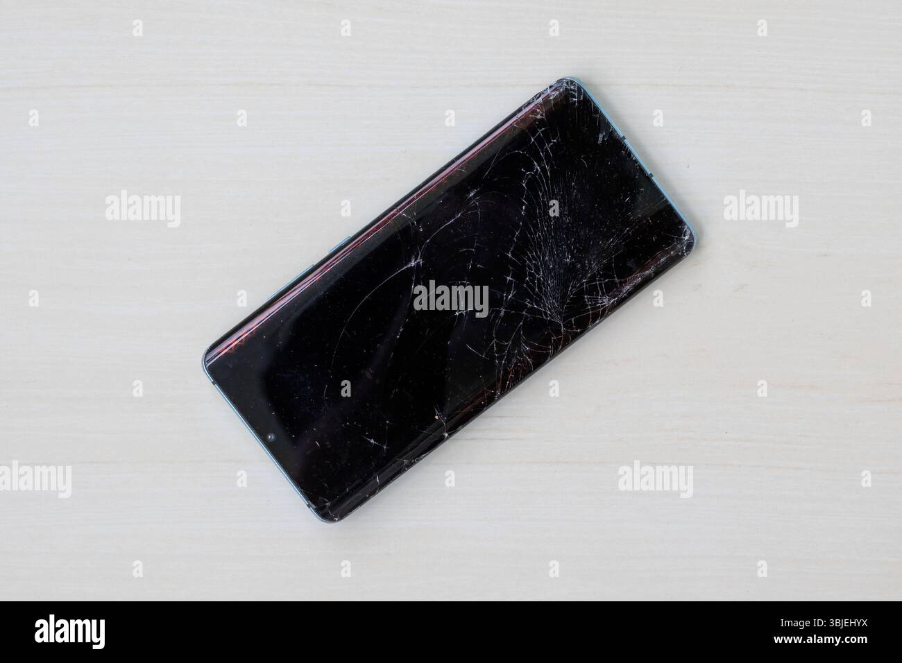 Smartphone con schermo incrinato su sfondo in legno. Vista dall'alto del display del telefono cellulare danneggiato. Telefono cellulare rotto da riparare. Foto Stock