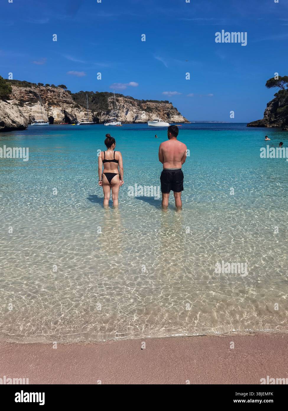 Minorca, España; Mayo 7 2025: Una coppia si trova pacificamente sulla riva di una spiaggia turchese incontaminata di Minorca. Foto Stock