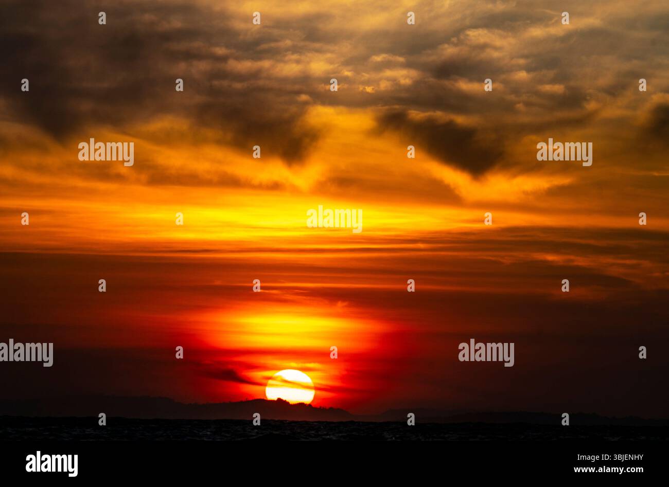 Uno splendido tramonto sull'oceano, caratterizzato da vivaci sfumature di arancione, giallo e rosso che si fondono in un cielo spettacolare pieno di nuvole. Foto Stock