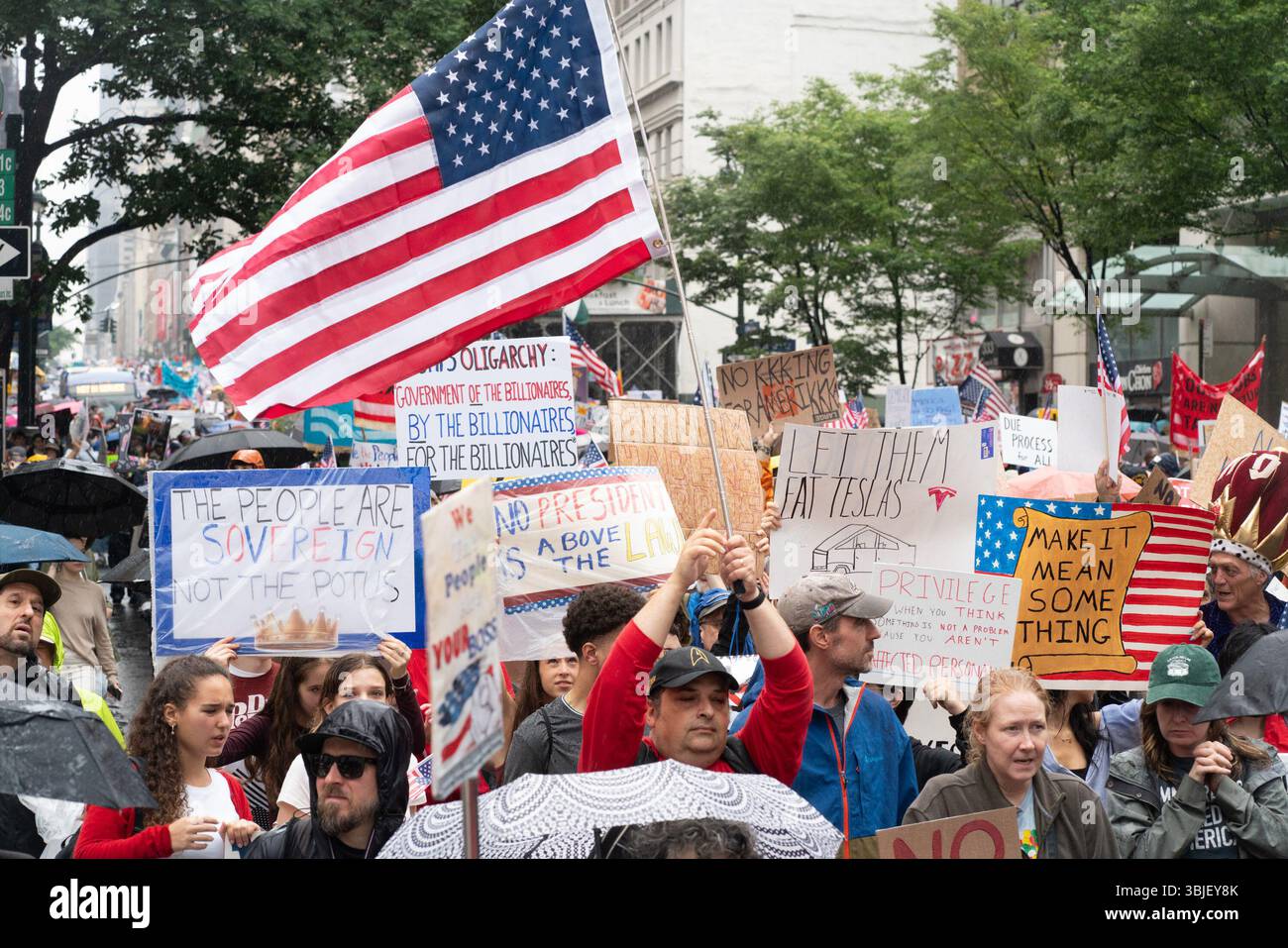 I manifestanti marciano sotto la pioggia tenendo bandiere e cartelli durante la protesta "No Kings Day" a New York City. Decine di migliaia hanno colpito le strade a livello nazionale per marciare contro il presidente Trump e le sue amministrazioni aumentando il dominio autocratico degli Stati Uniti. Il presidente ha celebrato il suo compleanno, che è il 14 luglio, ospitando una parata che espone i militari del paese a Washington DC, mentre la gente ha colpito le strade a livello nazionale per marciare contro il presidente Trump e la sua amministrazione aumentando il dominio autocratico. Il presidente ha celebrato il suo compleanno, che è il 14 luglio, ospitando una parata che mostra il conteggio Foto Stock