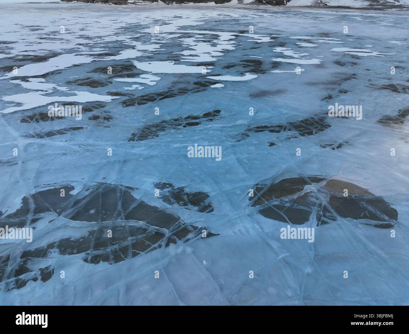 Vista aerea ravvicinata della superficie di un lago ghiacciato, rivelando intricati schemi di ghiaccio incrinato e macchie più scure esposte Foto Stock