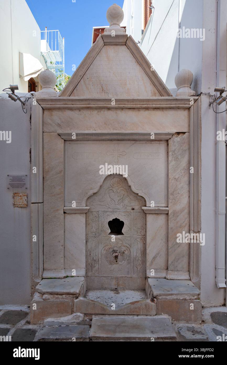Elegante fontana in marmo con dettagli scolpiti e iscrizione greca, un punto di riferimento neoclassico conservato nascosto negli stretti vicoli di Parikia, Paros. Foto Stock