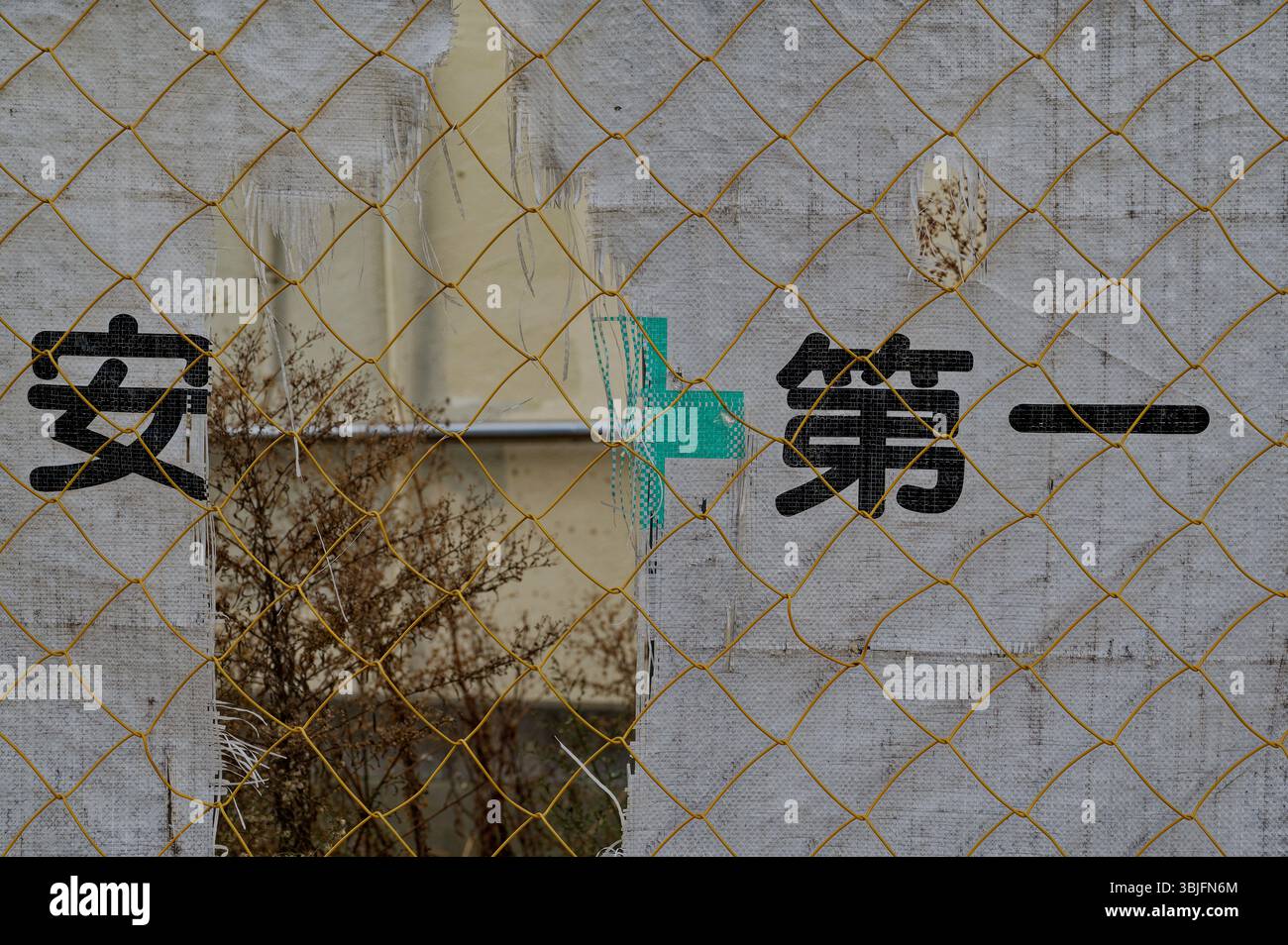 La rete di costruzione sbiadita dietro una recinzione metallica gialla riporta lo slogan di sicurezza “安全第一” (Safety First) in grassetto kanji nero Foto Stock