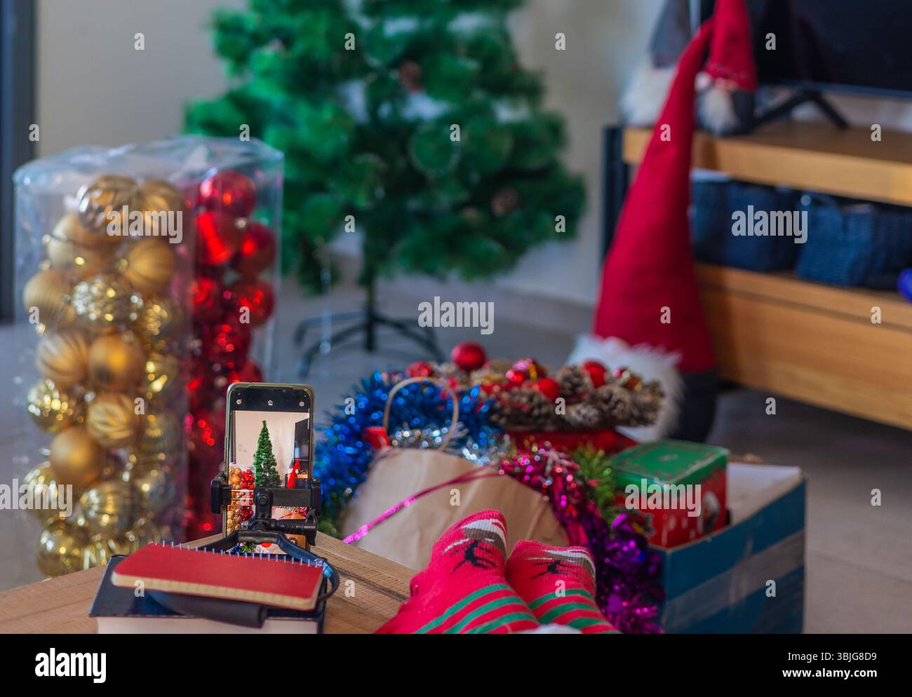 Primo piano della scena natalizia con albero di Natale artificiale, scatole di ornamenti, tinsel e regali che creano un'atmosfera accogliente per il Capodanno e le vacanze Foto Stock