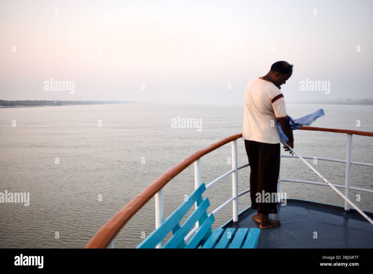 Un uomo a piedi nudi prepara l'attrezzatura al crepuscolo sul ponte DEL ML Bon Bibi mentre la nave da crociera si avvicina alla baia del Bengala attraverso i Sundarbans. Foto Stock