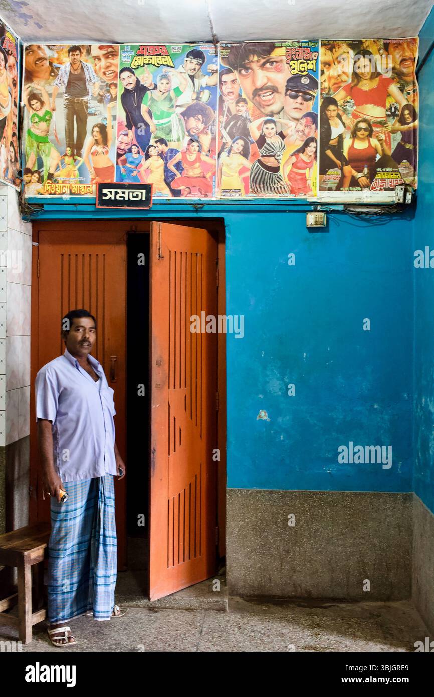 Un uomo si trova all'ingresso di una sala cinematografica a Jessore, Bangladesh, sotto vivaci poster di Dhallywood con azione, dramma e danza. Foto Stock