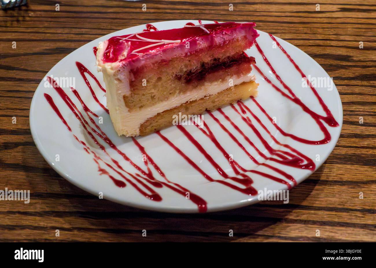 Una fetta di torta limoncello umida è condita con una vivace salsa di lamponi, che mescola agrumi e frutti di bosco dolci per un des rinfrescante ed elegante Foto Stock