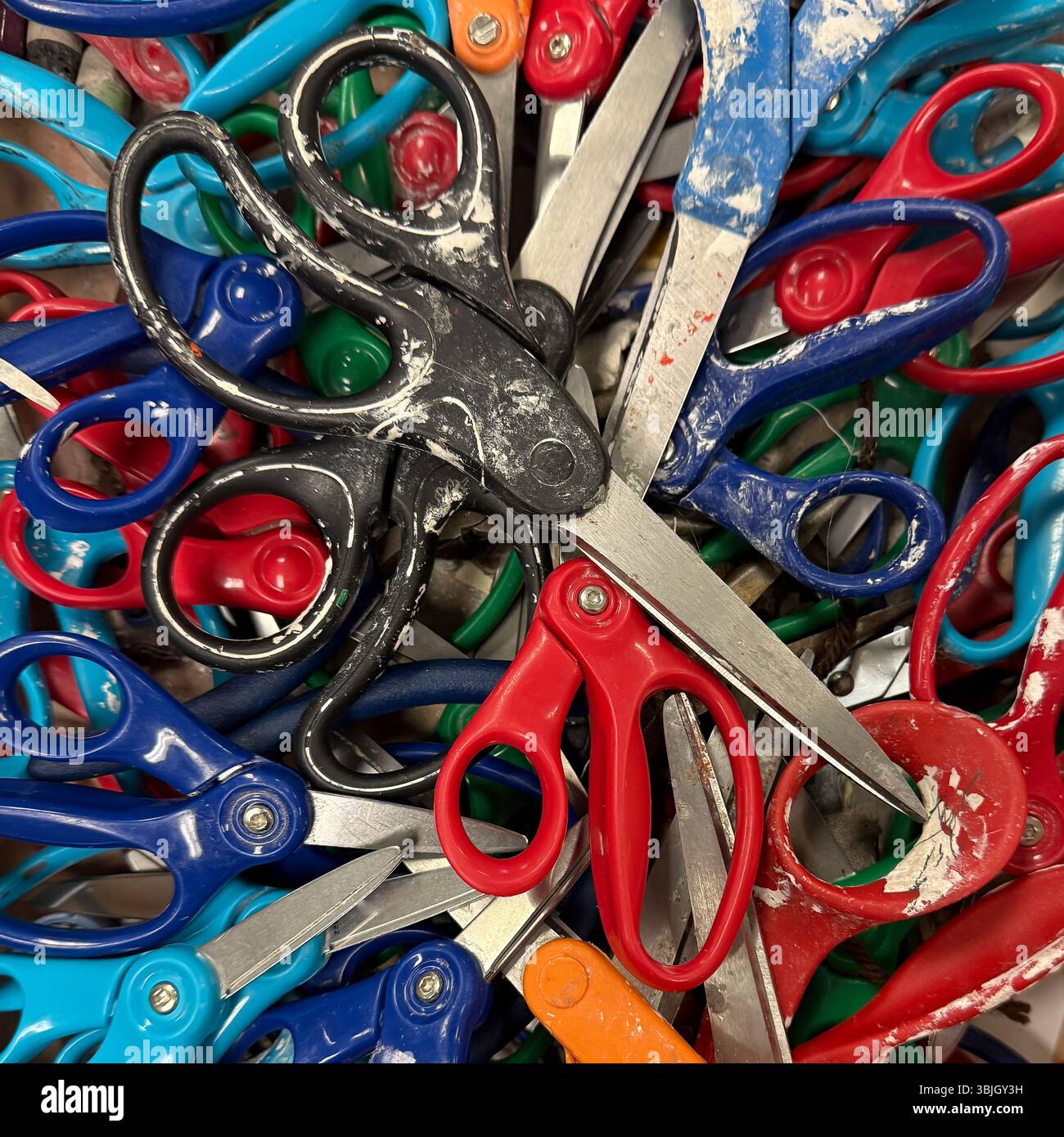 Foto a colori di una scatola di più forbici in plastica e acciaio inossidabile in una disposizione casuale. Foto Stock