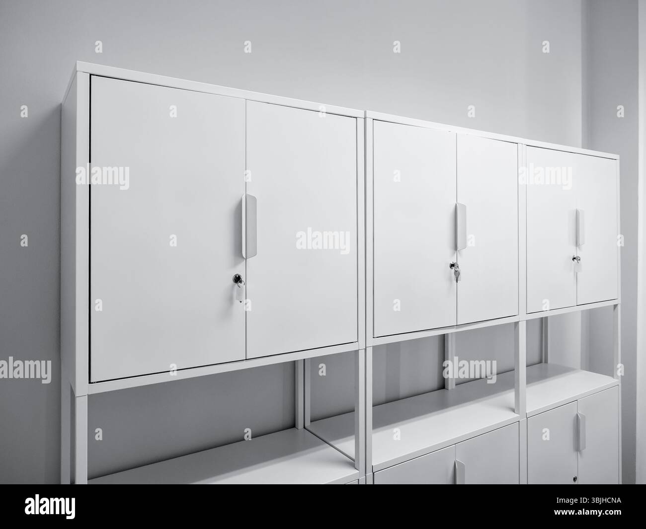 Tre armadietti da ufficio con porta a battente in acciaio bianco con serrature e ripiani impilabili, mobili in fila, collocati in camera bianca per i nuovi lavori di ufficio Foto Stock