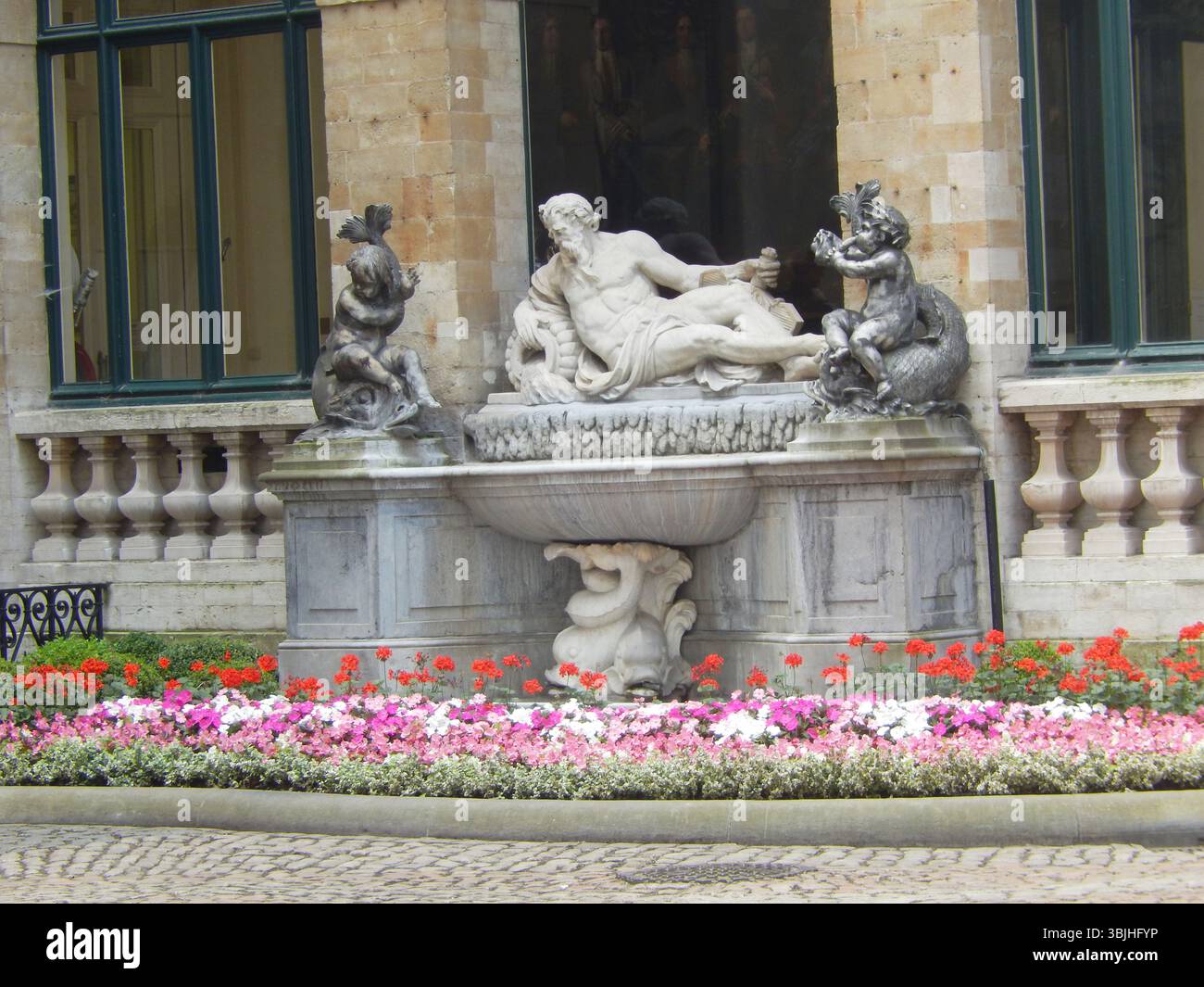 Elegante scultura in marmo della fontana circondata da un giardino di fiori in un ambiente storico. Mechelen, Belgio Foto Stock