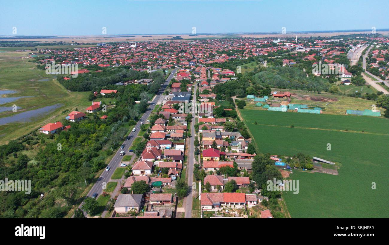 Vista aerea di un tranquillo villaggio rurale, case tradizionali, tetti rossi, strade rettilinee, vegetazione lussureggiante e terreni agricoli aperti. Ungheria, Balcani. Foto Stock