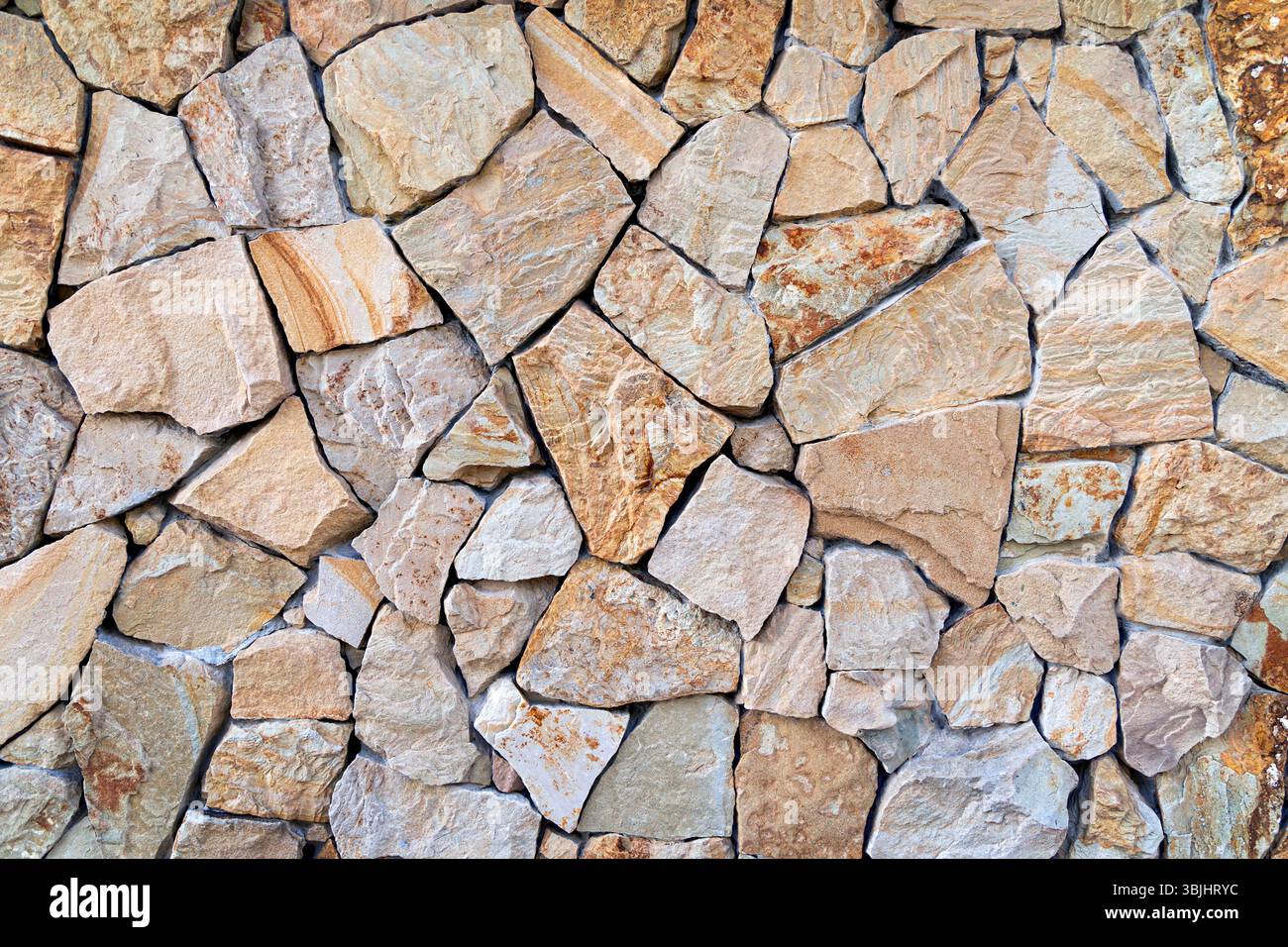 Muro in pietra con forme irregolari. Un'immagine dettagliata di un muro di pietra testurizzata composto da pietre di forma irregolare in varie tonalità di beige Foto Stock
