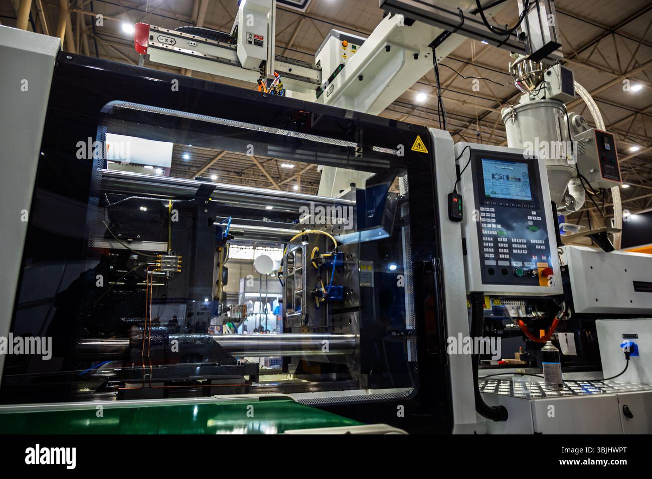 Primo piano di una macchina per lo stampaggio ad iniezione con un braccio robotico, che mostra gli intricati meccanismi interni e il pannello di controllo in un ambiente industriale, Highl Foto Stock