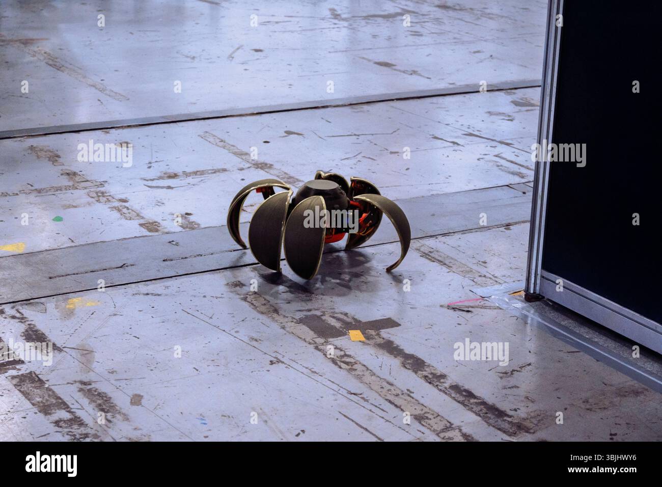 Piccolo robot metallico simile a un insetto con più gambe si stende su un pavimento sporco, mostrando tecnologia futuristica e design ingegneristico Foto Stock
