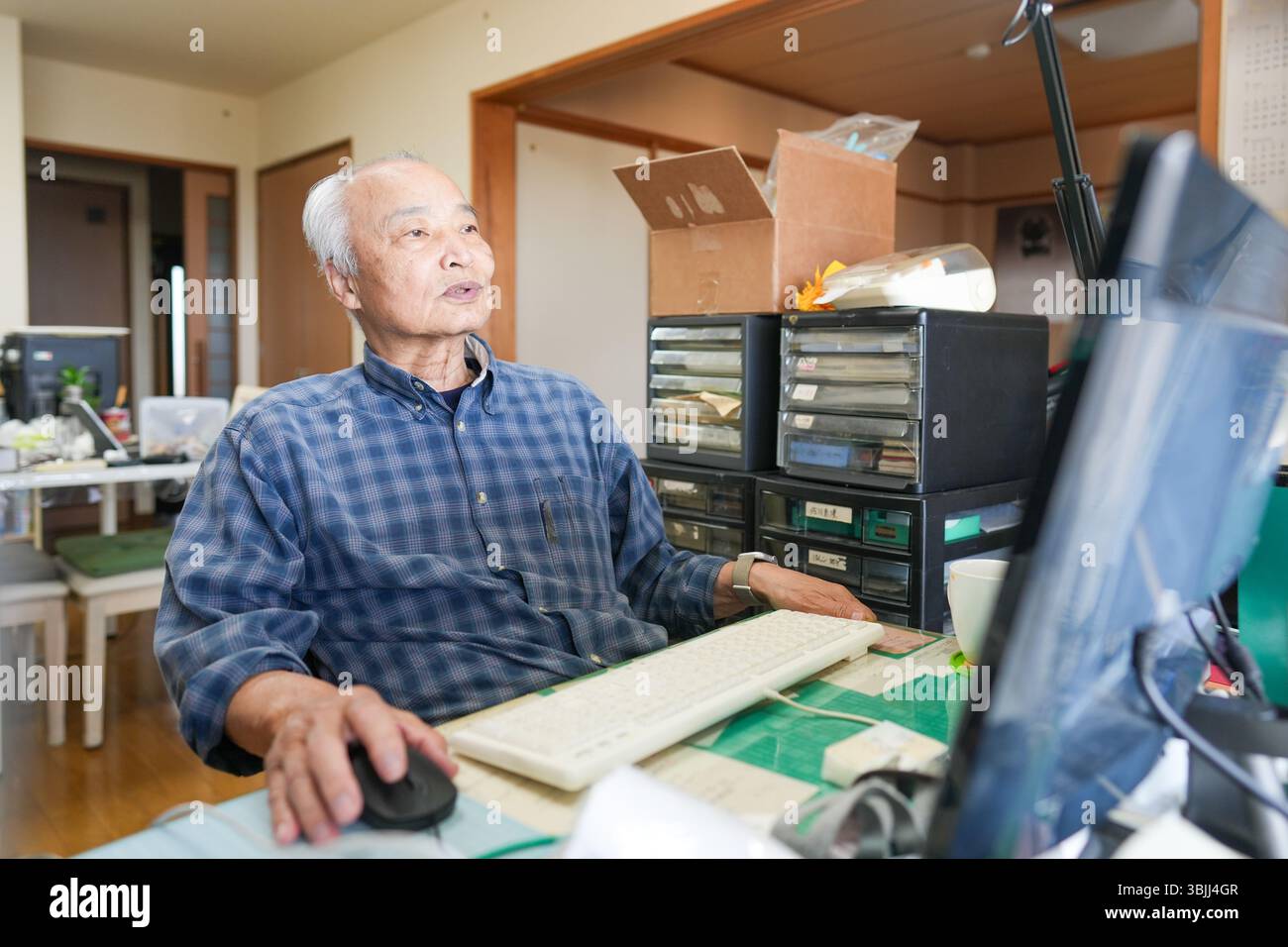 In Giappone, all'interno di un piccolo appartamento, un uomo giapponese alla fine degli anni '70 siede davanti a un computer, sorridente e chiacchierando, con una calda illuminazione interna c Foto Stock
