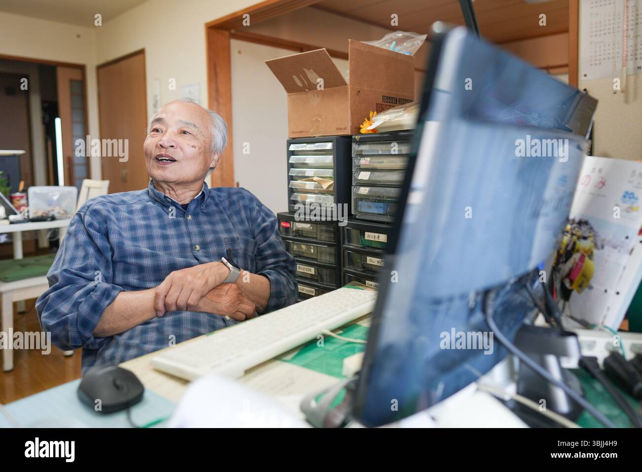 In Giappone, all'interno di un piccolo appartamento, un uomo giapponese alla fine degli anni '70 siede davanti a un computer, sorridente e chiacchierando, con una calda illuminazione interna c Foto Stock