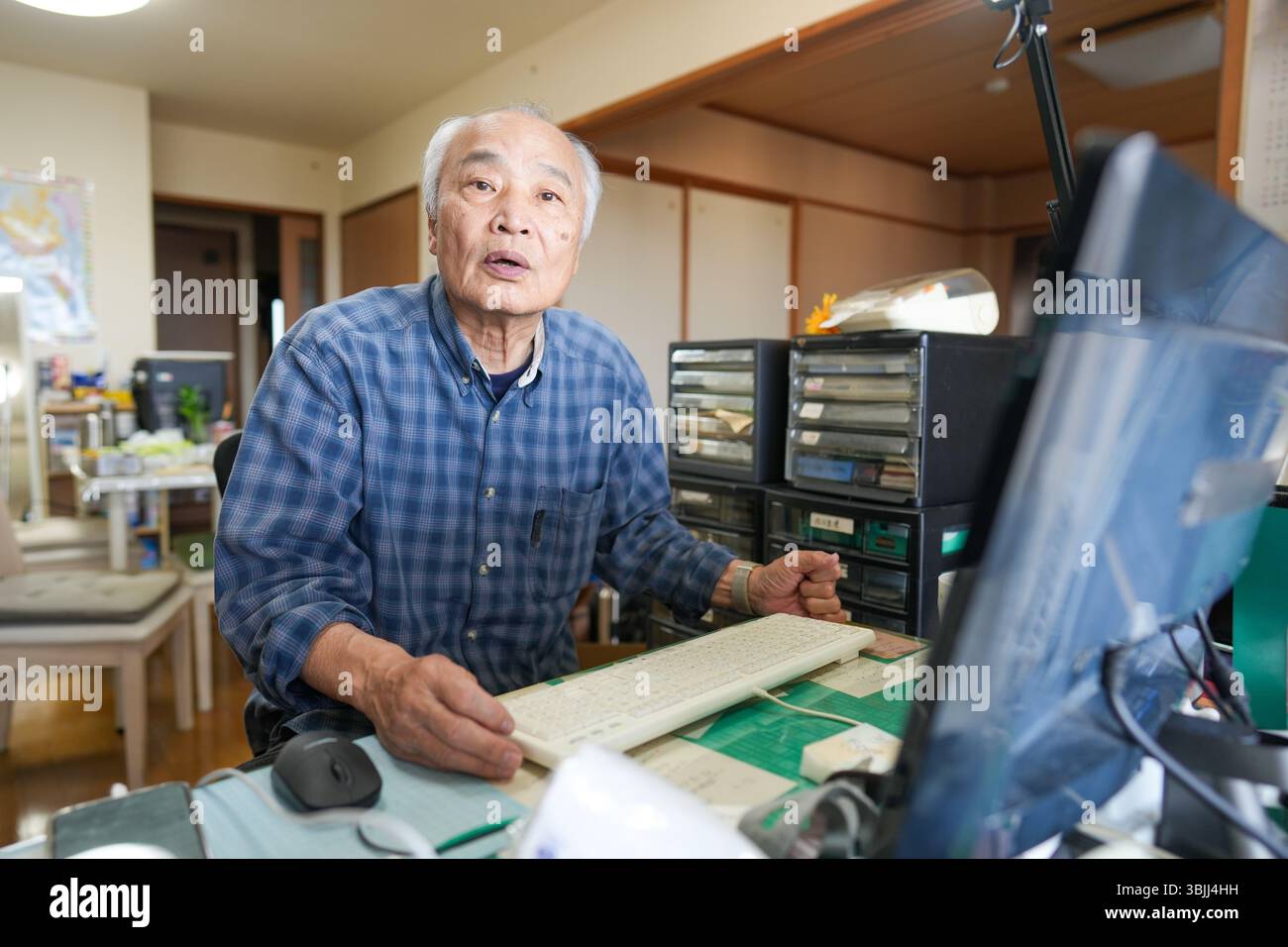 In Giappone, all'interno di un piccolo appartamento, un uomo giapponese alla fine degli anni '70 siede davanti a un computer, sorridente e chiacchierando, con una calda illuminazione interna c Foto Stock
