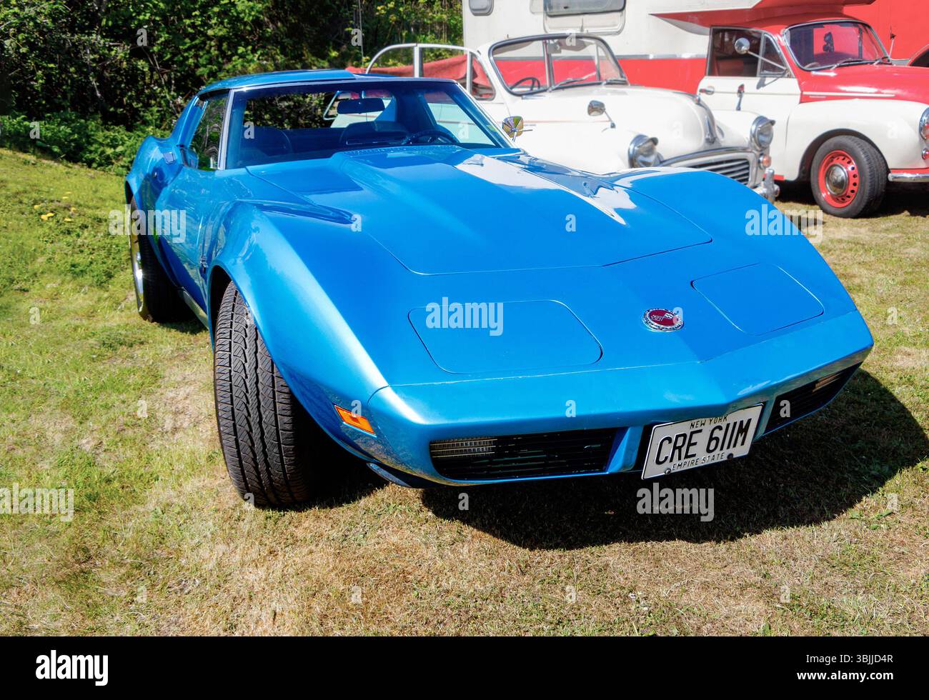Auto sportiva chevrolet in corvetta blu d'epoca in mostra in un'area erbosa con veicoli classici e un camper bianco sullo sfondo Foto Stock
