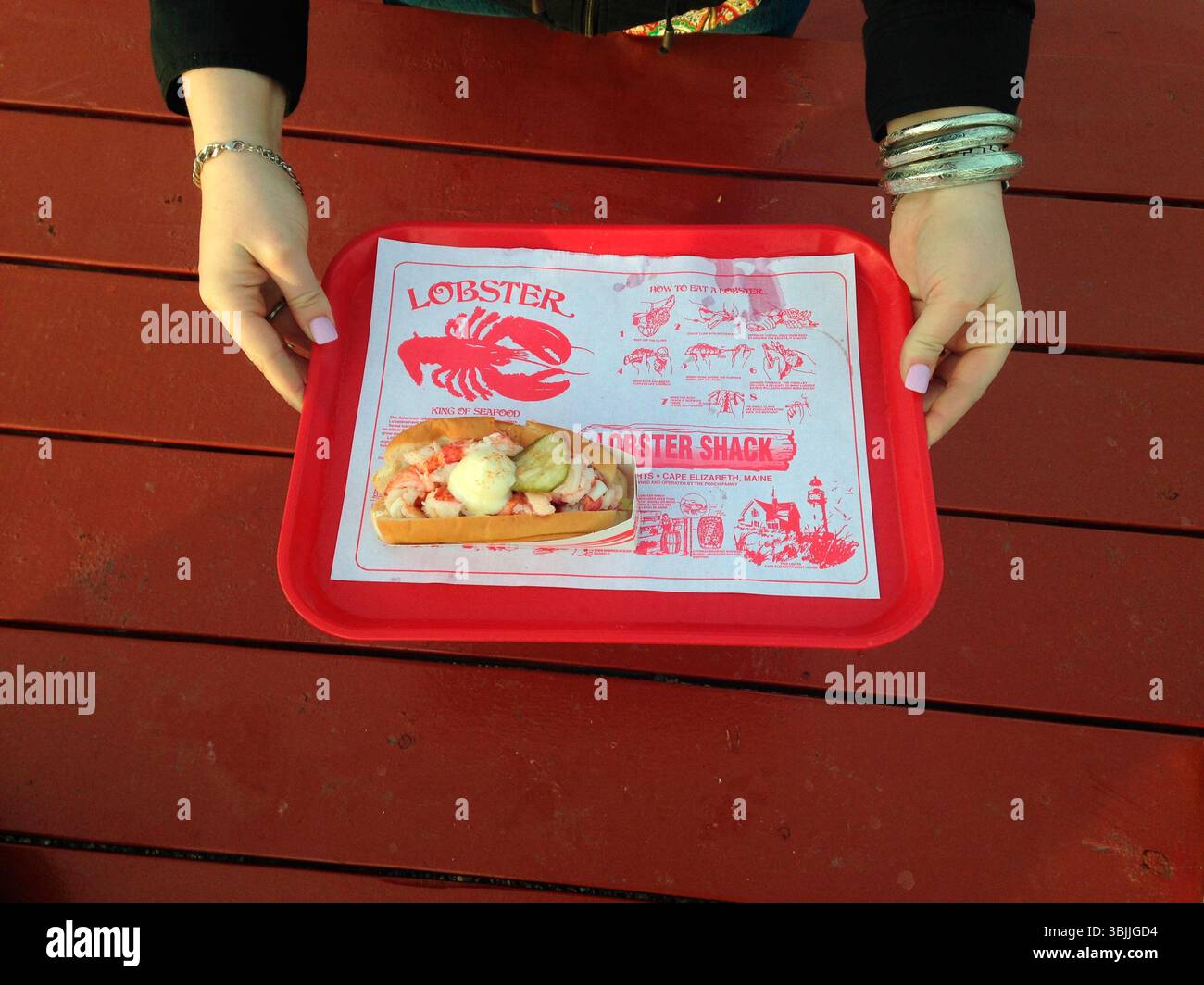 Donna che tiene in mano un vassoio e un rotolo di aragosta al Lobster Shack vicino a Two Lights, Cape Elizabeth, Maine. Foto Stock