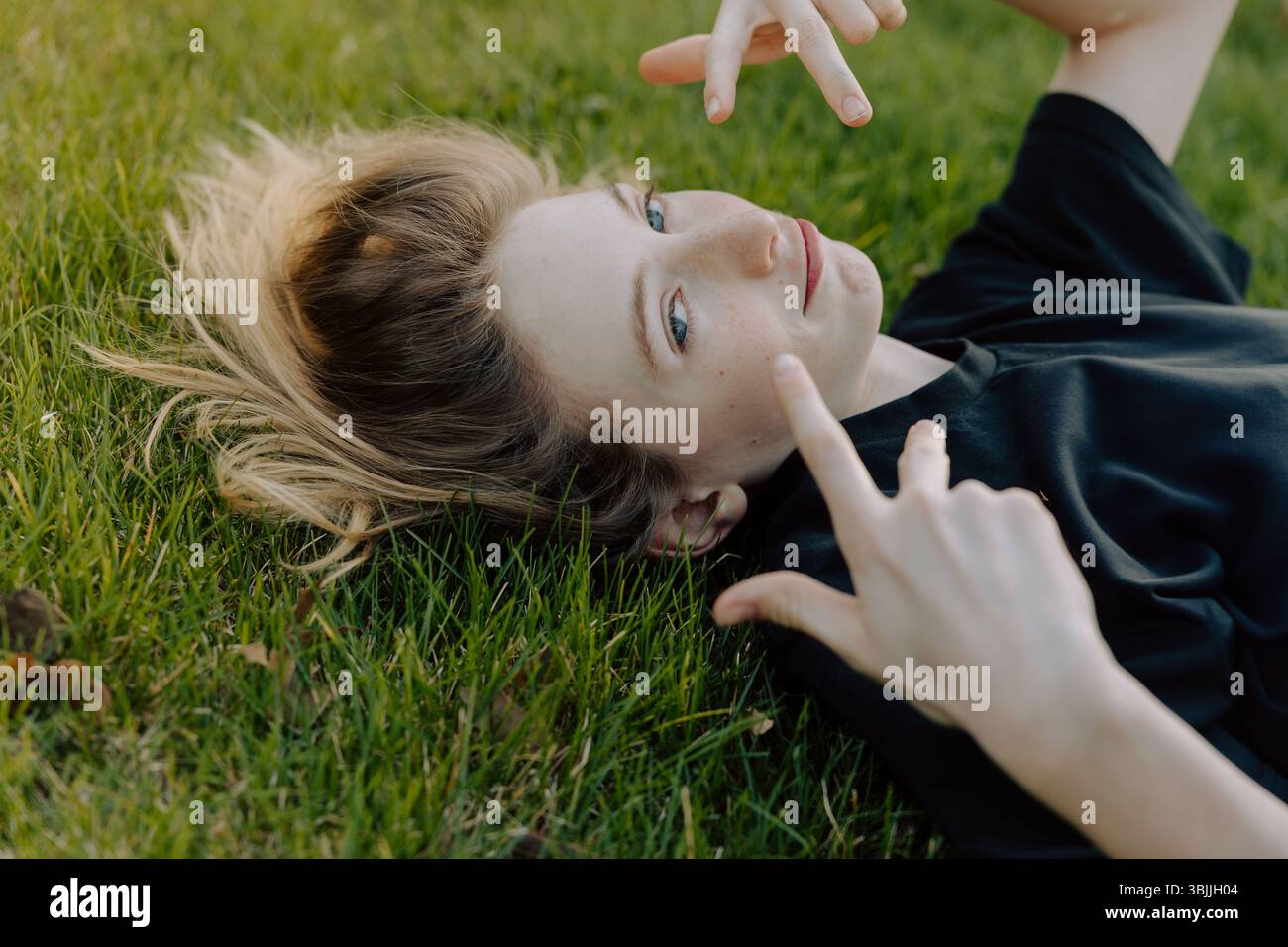 Adolescente steso sull'erba che fa gesti delle mani Foto Stock