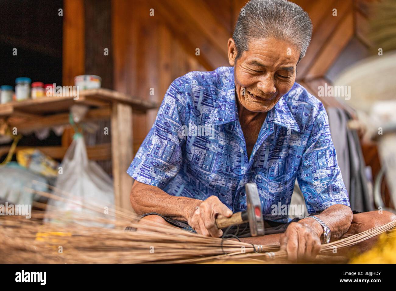 Sorridente artigiano thailandese che fissa saldamente le setole della scopa di cocco Foto Stock