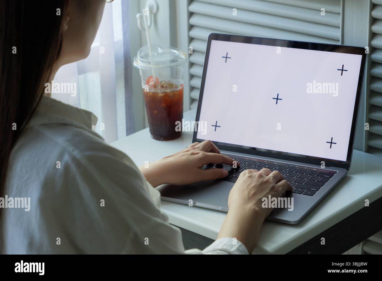 modello di schermo bianco vuoto per laptop. donna che utilizza la digitazione manuale su un computer portatile a casa per lavorare o divertirsi di giorno con un caffè ghiacciato sul tavolo Foto Stock