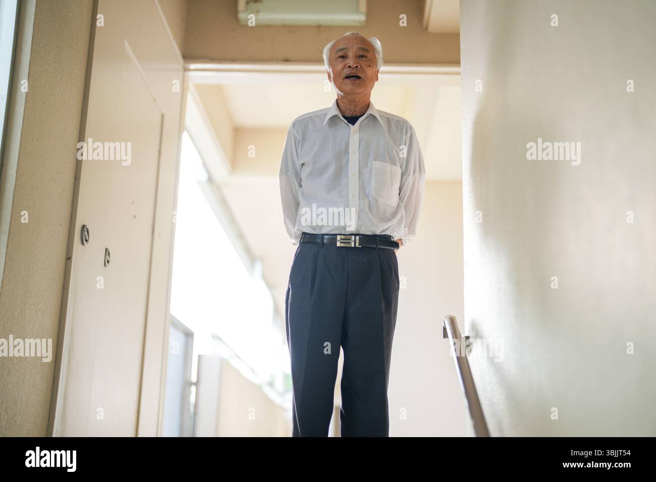 In un appartamento giapponese, un uomo giapponese alla fine degli anni '70, indossando una camicia bianca e un cappello bianco, si trova accanto alla ringhiera delle scale. Guarda avanti con calma Foto Stock