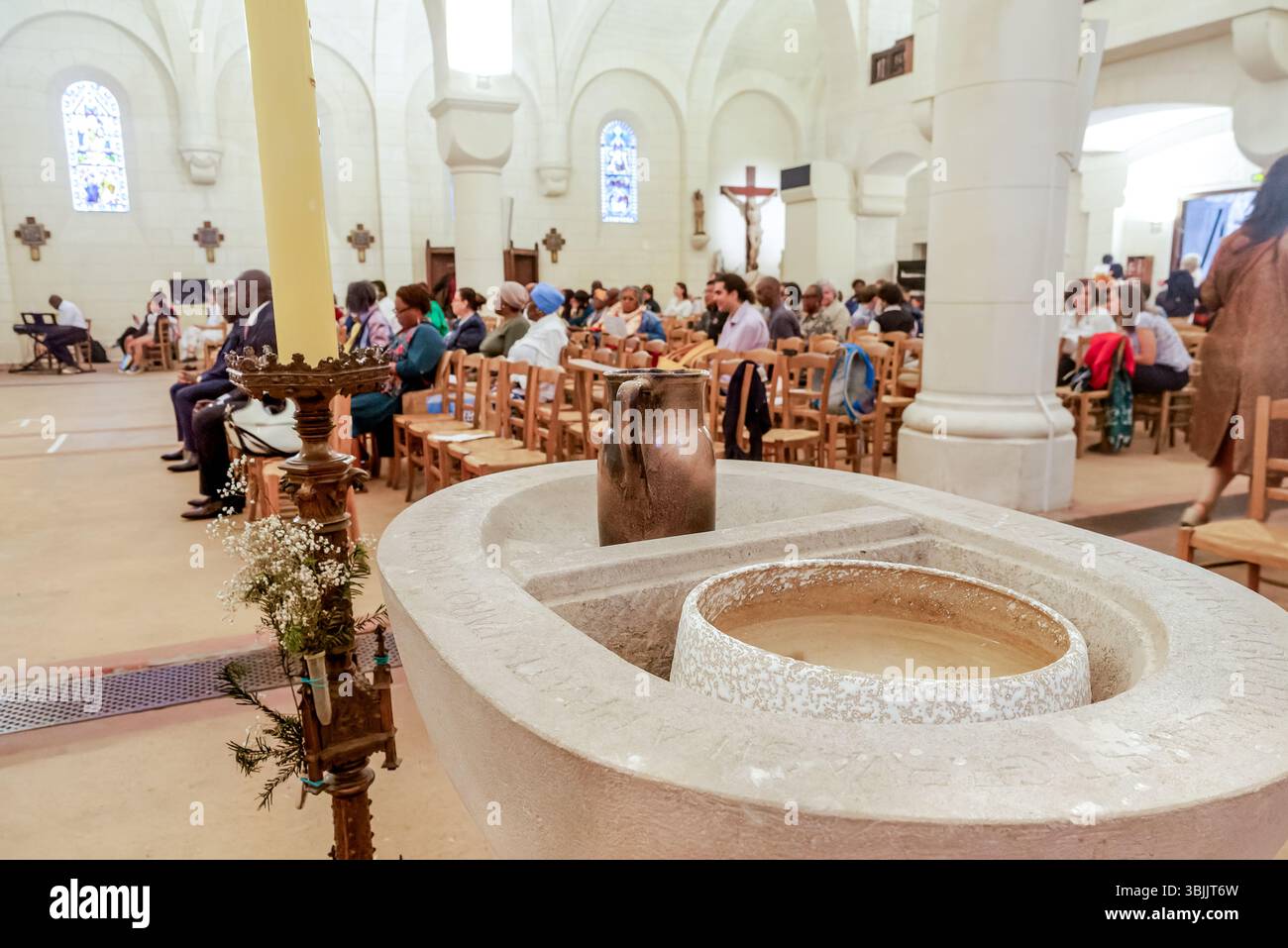 Fonte battesimale all'interno di una chiesa cattolica, con parrocchiani riuniti per una cerimonia di battesimo, che simboleggia la fede e il rinnovamento nella tradizione cristiana Foto Stock