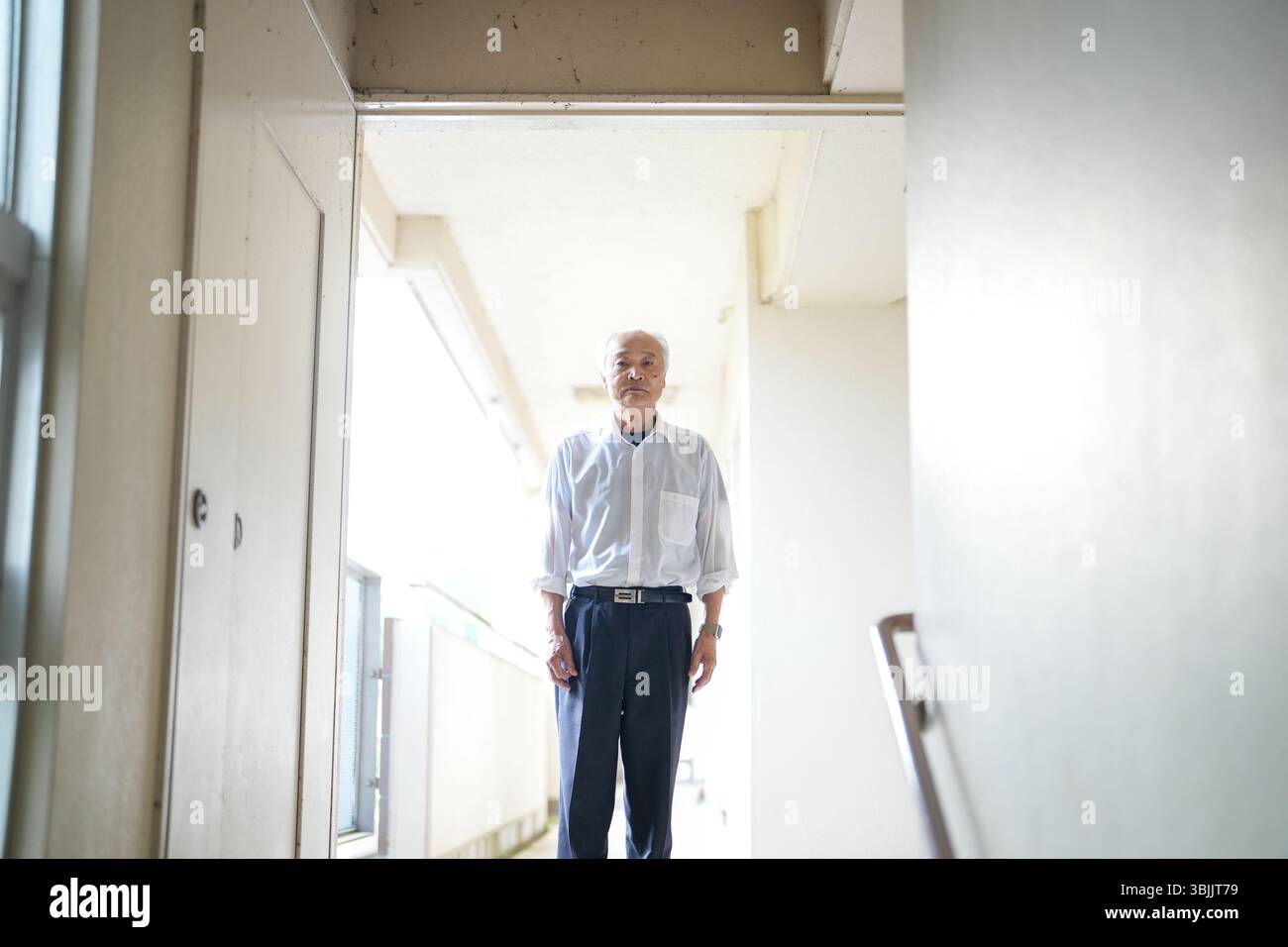 In un appartamento giapponese, un uomo giapponese alla fine degli anni '70, indossando una camicia bianca e un cappello bianco, si trova accanto alla ringhiera delle scale. Guarda avanti con calma Foto Stock