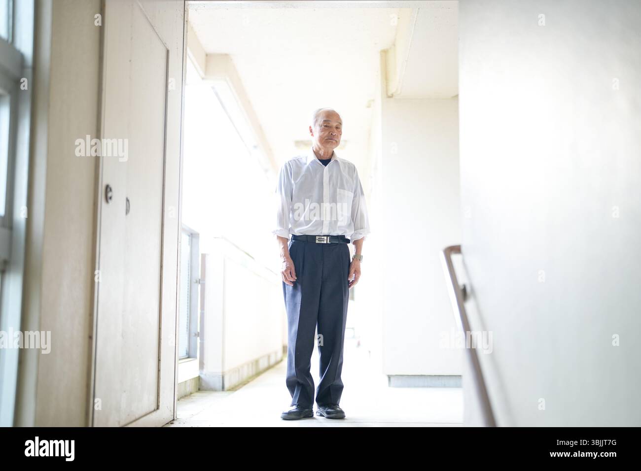 In un appartamento giapponese, un uomo giapponese alla fine degli anni '70, indossando una camicia bianca e un cappello bianco, si trova accanto alla ringhiera delle scale. Guarda avanti con calma Foto Stock