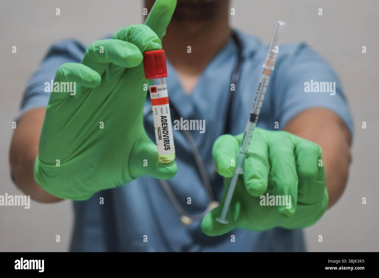 Testo Adenovirus vaccino di è scritto su una bottiglia con sfondo di un medico con una siringa in una maschera di guanti medici. Concetto medico Foto Stock