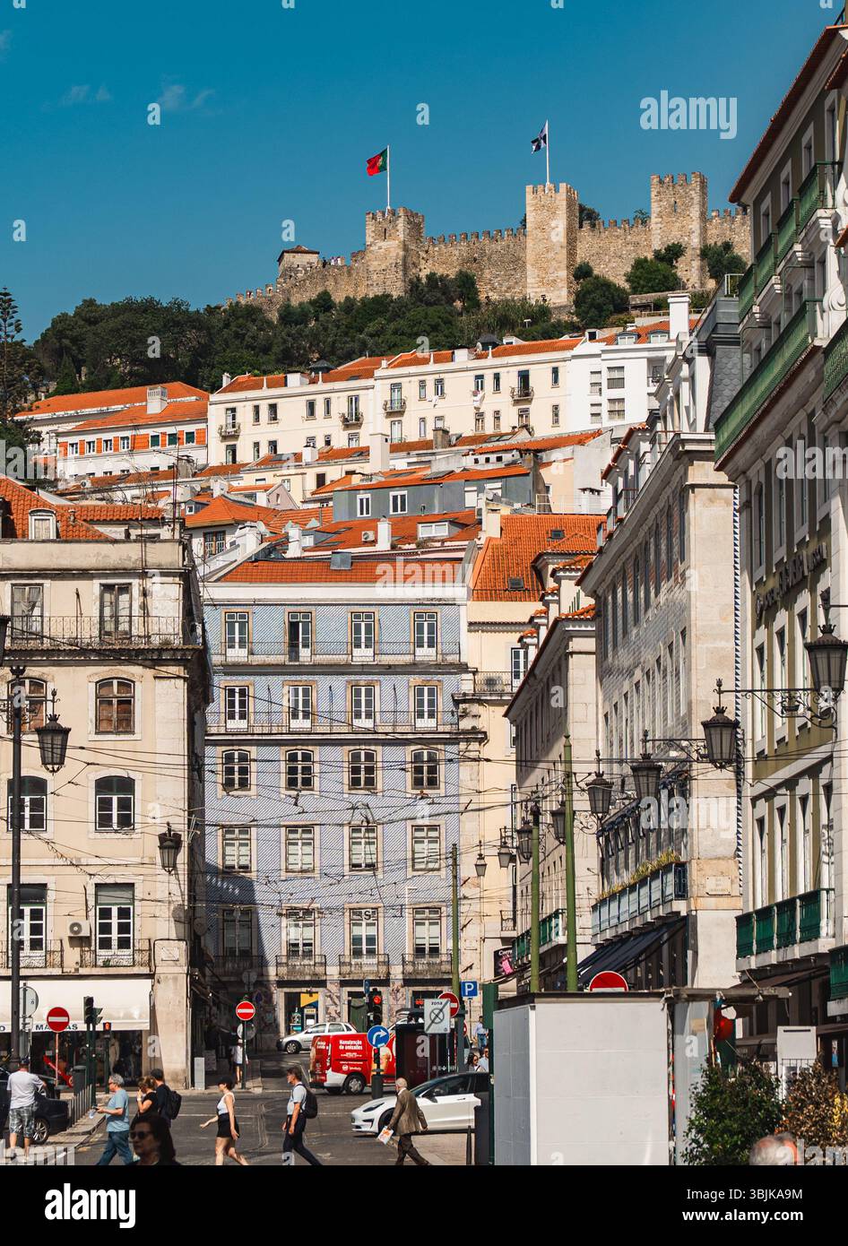 Vivace vita cittadina e architettura storica sotto il Castello di Sao Jorge, catturando l'atmosfera urbana quotidiana e l'iconico skyline di Lisbona. Lisbona, Portogallo - 11 giugno 2025 Foto Stock