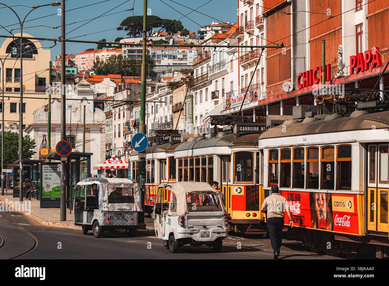 I classici tram gialli e tuk-tuk navigano in una vivace strada di Lisbona, catturando la vita urbana quotidiana e l'architettura locale. Lisbona, Portogallo - 11 giugno 2025 Foto Stock