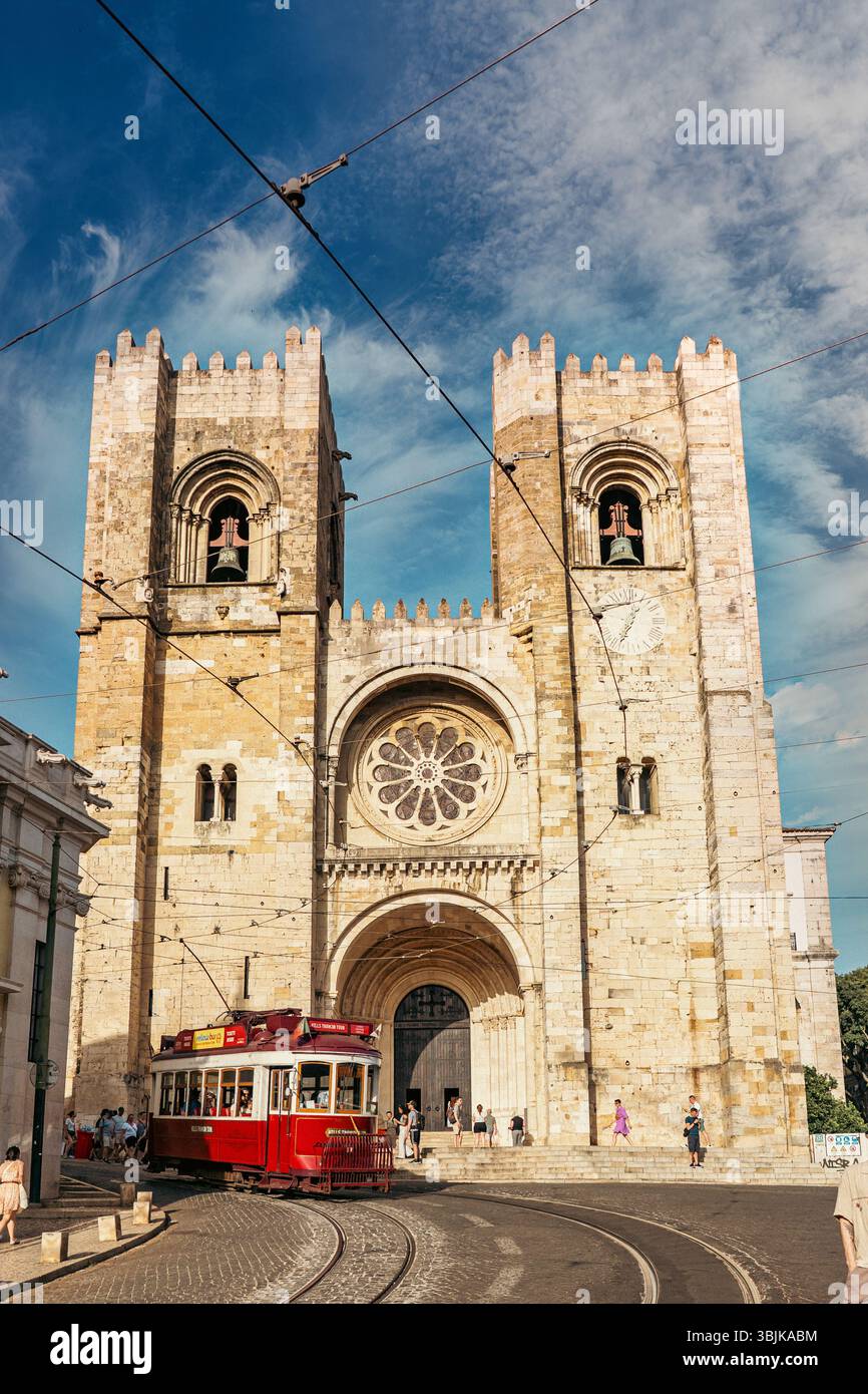 La storica cattedrale di Lisbona si erge alta mentre passa un classico tram rosso, catturando l'atmosfera vibrante della città. Lisbona, Portogallo - 11 giugno 2025 Foto Stock