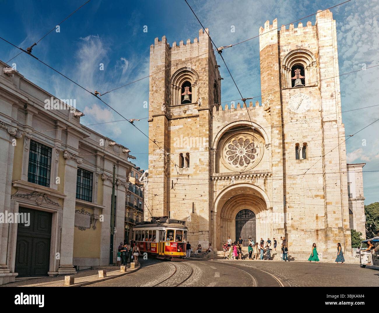 La storica cattedrale di Lisbona con l'iconico tram giallo e i turisti, catturando la vivace vita e l'architettura della città. Lisbona, Portogallo - 11 giugno 2025 Foto Stock