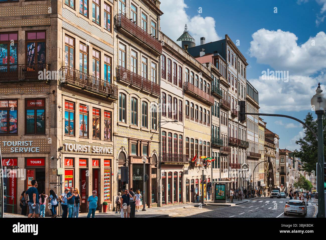 Vivace strada cittadina con tradizionali edifici piastrellati, servizi turistici e persone che esplorano il centro storico. Porto, Portogallo - 11 giugno 2025 Foto Stock
