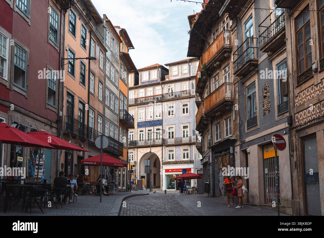 Vecchi edifici colorati, caffetterie all'aperto e persone che si godono una strada vivace nel cuore del centro storico di Porto. Porto, Portogallo - 11 giugno 2025 Foto Stock