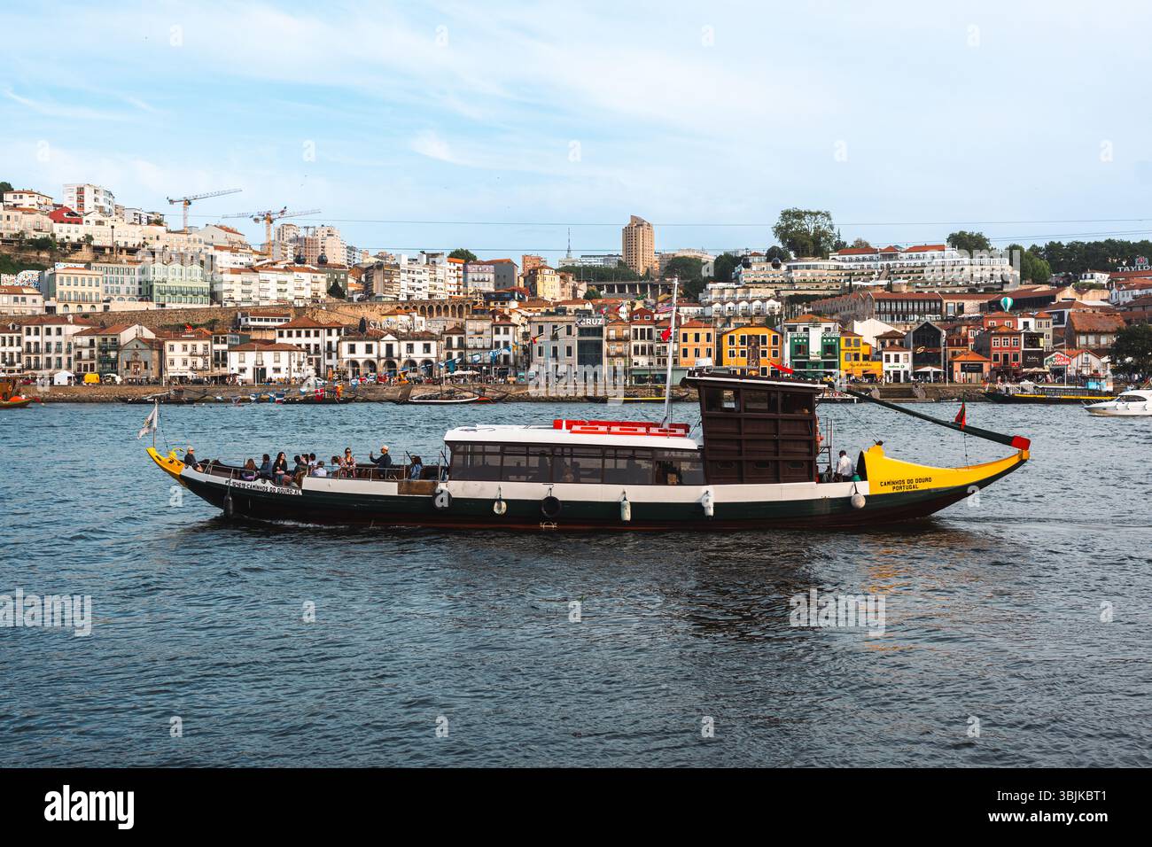 Una classica barca rabelo piena di turisti naviga lungo il fiume Douro, con edifici colorati lungo il fiume Porto sullo sfondo. Porto, Portogallo - 11 giugno 2025 Foto Stock