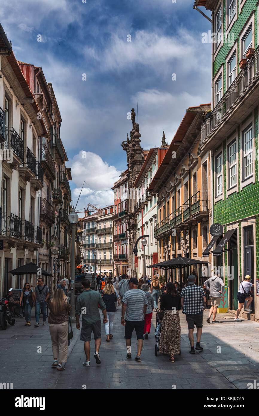 I turisti e la gente del posto passeggiano lungo una vivace e colorata strada costeggiata da edifici tradizionali nel centro storico di Porto. Porto, Portogallo - 11 giugno 2025 Foto Stock